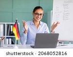 Small photo of E-learning with teacher, social distancing, new normal. Happy female tutor giving German language lesson online, using laptop. Young lecturer explaining grammar rules to students on internet