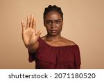 Young angry african american woman in casual outfit making the hand stop sign against beige studio background, closeup, copy space. Stop abuse, discrimination, violence concept