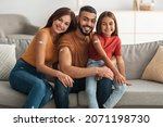 Small photo of Coronavirus Vaccination Advert. Happy Vaccinated Family Of Three People Showing Arm With Sticking Plaster After Covid-19 Vaccine Vax Injection Posing Sitting On Couch In Living Room, Smiling To Camera