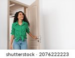 Small photo of Wow. Cheerful lady walking in modern flat, entering new home, happy young female standing in doorway of apartment, holding doorknob handle looking at design interior, coming inside, free copy space