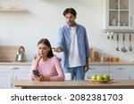 Small photo of Unhappy millennial caucasian husband swears wife in minimalist kitchen interior. Gadget and social networks addiction, treason, crisis and problems. Conflict, depression and stress at home, free space