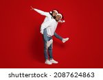 Loving african american millennial couple having fun together on red studio background, celebrating Christmas and New Year 2022, wearing Santa hats, doing piggyback, full size shot, copy space