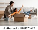 Small photo of Playful young Asian couple having fun in their home on relocation day. Millennial woman and her boyfriend playing together with carton box while moving to new apartment