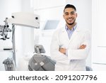 Small photo of Dental Center. Portrait Of Smiling Middle Eastern Dentist Doctor Posing At Workplace, Handsome Arab Stomatologist Standing With Folded Arms In Modern Clinic Interior, Ready For Check Up With Patient