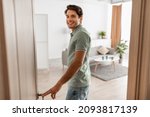 Small photo of Portrait of excited young man walking in his apartment, entering new home and looking back at camera, happy young guy standing in doorway of modern flat, coming inside, selective focus