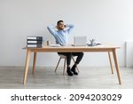 Taking Break. Smiling young Arab man relaxing on chair sitting at table and resting, using pc laptop, happy millennial male leaning back at workplace, enjoying his job, feeling pleased and satisfied