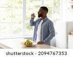 Small photo of Calm millennial african american bearded man with closed eyes drinks water from glass in kitchen interior with apples on window background. Thirst, aqua balance, healthy nutrition and hydration