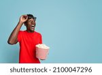 Small photo of Cinema Offer. Excited Black Guy With Popcorn Bucket In Hands Looking At Copy Space With Amazement, Dazed Young African American Man Taking Off 3d Glasses, Emotionally Reacting To Movie, Panorama