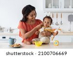 Small photo of Baby Weaning. Caring Black Mother Feeding Little Toddler Son From Spoon In Kitchen, Loving African American Mommy Giving Porridge Or Mash Fruit Puree To Cute Little Child At Home, Closeup Shot