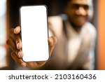 Small photo of Great offer. Black man showing mew modern smartphone with big white blank screen for application or website design, mockup, copy space, closeup