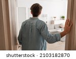 Small photo of Back rear view of unrecognizable young man walking in his apartment, entering new home, casual guy standing in doorway of modern flat, looking at design interior, coming inside, selective focus