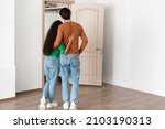 Rear back view of young couple hugging looking at open door together, welcoming inviting guests to enter home, guy and lady standing in doorway of modern flat, waiting for visitor friends to come in