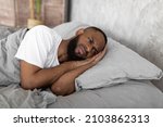 Small photo of Depression Concept. Portrait of upset African American man lying in bed in the morning and thinking. Sad black male feeling lonely or stressed, suffering from lack of sleep, distraught