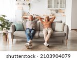 Small photo of Happy Mature Couple Sitting On Couch Relaxing And Resting At Home, Holding Hands Behind Head, Enjoying Comfort Of Their House. Relaxed Senior Spouses Having Lazy Weekend Indoors. Full Length