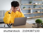 Small photo of Stressed Young Asian Man Touching Temples Grabbing Head Having Problem At Workplace Sitting At Desk Looking At Laptop Screen In Home Office. Tiredness And Entrepreneurship Issues, Headache Concept