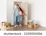 Housing Concept. Happy couple walking in empty house with cardboard carton boxes on floor, young family moving into new apartment after buying house, excited guy and lady hugging, looking around flat