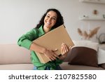 Delivery Service. Happy Shopaholic Lady Hugging Cardboard Box After Receiving Delivered Parcel With Products Sitting On Sofa At Home. Contented Buyer, Shopaholism And Commerce Concept