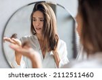 Hairloss Concept. Worried Young Woman Holding Bunch Of Fallen Hair In Hand While Standing Near Mirror In Bathroom, Stressed Beautiful Lady Suffering Alopecia Or Health Problems, Selective Focus