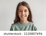 Small photo of Headshot Of Happy Girl Smiling Looking At Camera Posing With Loose Hair Wearing Casual Clothes Over Gray Studio Background. Kids Fashion In Preteen Age Concept. Front View Shot
