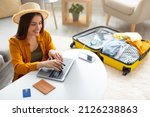 Happy young woman planning vacation travel with laptop pc, reading tourist blog online, booking tickets or hotel room on web, getting ready for abroad journey at home, free space