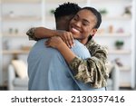 Closeup portrait of cheerful black female soldier lady in camouflage uniform hugging her boyfriend, home interior. Military wife came back from army, embracing her loving husband, finally together