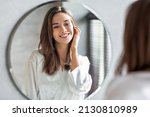 Small photo of Beauty Concept. Portrait Of Attractive Happy Woman Looking At Mirror In Bathroom, Beautiful Millennial Lady Wearing White Silk Robe Smiling To Reflection, Enjoying Her Appearance, Selective Focus