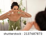 Small photo of Lovely young woman making lymphatic drainage facial self massage near mirror at home, free space. Beautiful millennial female doing domestic skin care treatmenrt at bathroom