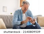 Small photo of Poor Eyesight In Older Age, Macular Degeneration Concept. Confused Mature Male In Eyeglasses Squinting Eyes Reading Message On Cell Phone Having Ophtalmic Issue Problems With Vision Sitting On Sofa