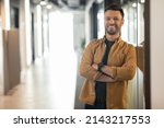 Successful Entrepreneurship. Happy Businessman Smiling To Camera Posing Crossing Hands Standing In Doorway Of Modern Office. Employment And Business Career Concept