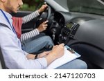 Small photo of Serious young muslim guy teacher taking driving test from woman in hijab at steering wheel driving car, cropped. Mentor teaches student to drive, driving class and good mark. Education and study