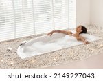Relaxation and wellness concept. Full length of pretty young woman taking foamy bath, lying with closed eyes in bathtub at home, free space. Attractive millennial lady bathing at luxury hotel