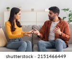 Small photo of Angry Arabic Spouses Having Quarrel Arguing Looking At Each Other Sitting On Couch At Home. Domestic Violence And Abuse. Couple Struggling From Marital Crisis Concept