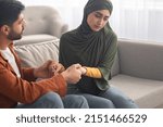 Small photo of Marital Crisis. Unhappy Middle Eastern Couple Holding Hands Sitting Together On Sofa Indoors. Bad Relationship, Forced Marriage Problem And Family Conflicts Concept. Selective Focus
