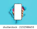 Mobile App, Great Offer. Black male hand holding smartphone with white empty screen showing device close up to camera breaking through blue paper sheet. Gadget display with free copy space, mock up