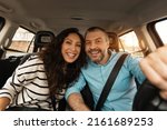 Small photo of Front portrait of smiling beautiful couple sitting in modern luxury car, happy excited young man and woman posing looking at camera, enjoying road trip or buying new car, sun flare, windshield view