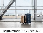 Two Stylish Plastic Luggage Suitcases Standing Near Panoramic Window At Airport, Blue And Beige Travel Bags Waiting In Terminal, Creative Shot For Transportration And Travelling Concept, Copy Space