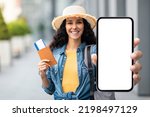 Small photo of Happy attractive millennial brunette lady in straw hat tourist holding passport with flight tickets and cell phone with white blank screen, showing nice mobile app for travellers, mockup