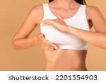 Breast self-screening concept. Young woman in white bra making checkup for cancer prevention, beige studio background, closeup, cropped