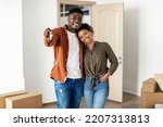 Family Housing. African American Millennial Couple Showing Key Posing Embracing In New House Among Moving Boxes. Real Estate Buyers Standing At Their Own Home, Smiling To Camera