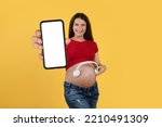 Music App. Cheerful Young Pregnant Woman Holding Wireless Headphones Near Belly And Showing Big Blank Smartphone At Camera While Standing Isolated Over Yellow Background, Collage, Mockup