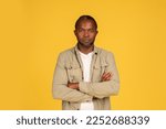 Small photo of Serious confident middle aged african american male in casual crossed arms on chest, looking at camera, isolated on yellow background, studio. Lifestyle, emotions, discontent, conflict and negative