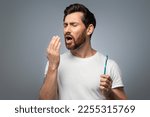Bad breath. Handsome middle aged man checking his breath with his hand, blowing to it, standing over grey background. Bad smell from the mouth, toothache, having problems with teeth