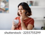 Small photo of Sensitive Teeth. Young arab woman drinking water with ice and touching her cheek, sick middle eastern female frowning and rubbing inflamed area, suffering dental pain, emotionally reacting to cold