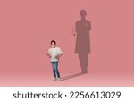 Small photo of Childhood dreams concept. Cool cheerful school aged asian girl dreaming to become a doctor, shadow of female doc behind her, kid posing over pink wall studio background, collage, copy space