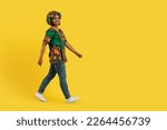 Small photo of Cheerful happy pretty young black woman in traditional outwear turban and accessories walking towards copy space for advertisement, isolated on yellow studio background, full length shot