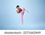 Black female trainer showing kick exercise for self defence by legs on blue studio background, copy space. African american woman training in sportswear in studio