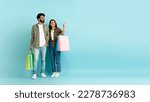 Small photo of Sale, black friday, discount. Loving happy millennial multicultural couple in casual go shopping together, pretty eastern woman showing her handsome arab husband copy space, blue background, banner