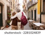 Small photo of Vacation Tour Offer. Back View Of Senior Couple Hugging And Carrying Backpack Walking On Lisbon Street, Enjoying Sightseeing Outdoors. Travel And Tourism In Europe Concept