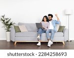 Small photo of Positive attractive interracial young couple middle eastern man and indian woman using computer at home, cheerful spouses planning weekend or vacation, booking cheap tickets on Internet, copy space