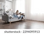 Candid shot of happy young eastern couple chilling on couch at home, using gadgets smartphone and digital tablet, indian man and woman relaxing at weekend together, copy space, full length